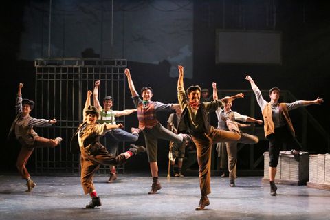 Newsies dancing in front of the gates of the newspaper office.
