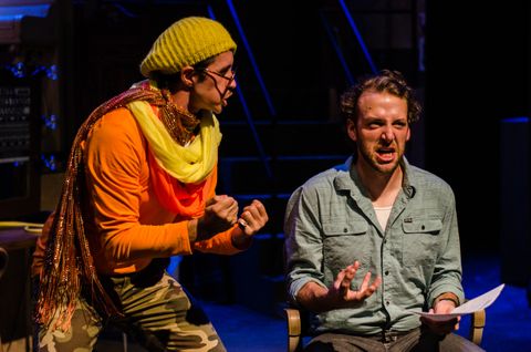 A cloeser view of two actors from the previous image. The dirctor is working with one of the actors. They are lit by warm front light and dim blue back light.