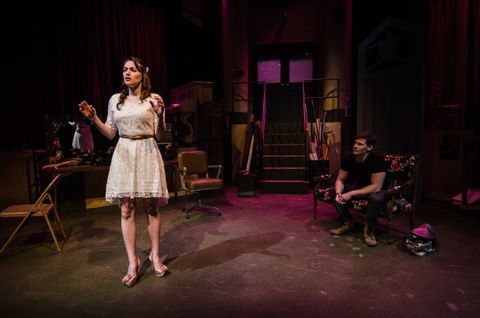 A wider view of the previous image. The actress in a white dress is scuplted by warm front light from one side and a cool fill from the other.  The stage manager sits on a love seat in semidarkness.